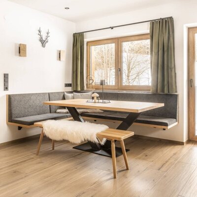 Dining area with a wooden table, corner bench, wooden floor, and window view.