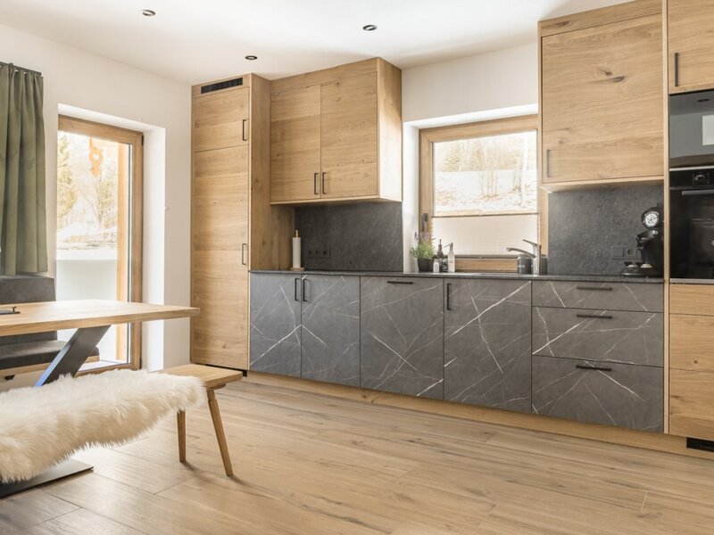 Modern kitchen with wooden elements, dark countertops, integrated appliances, and a dining table with benches.