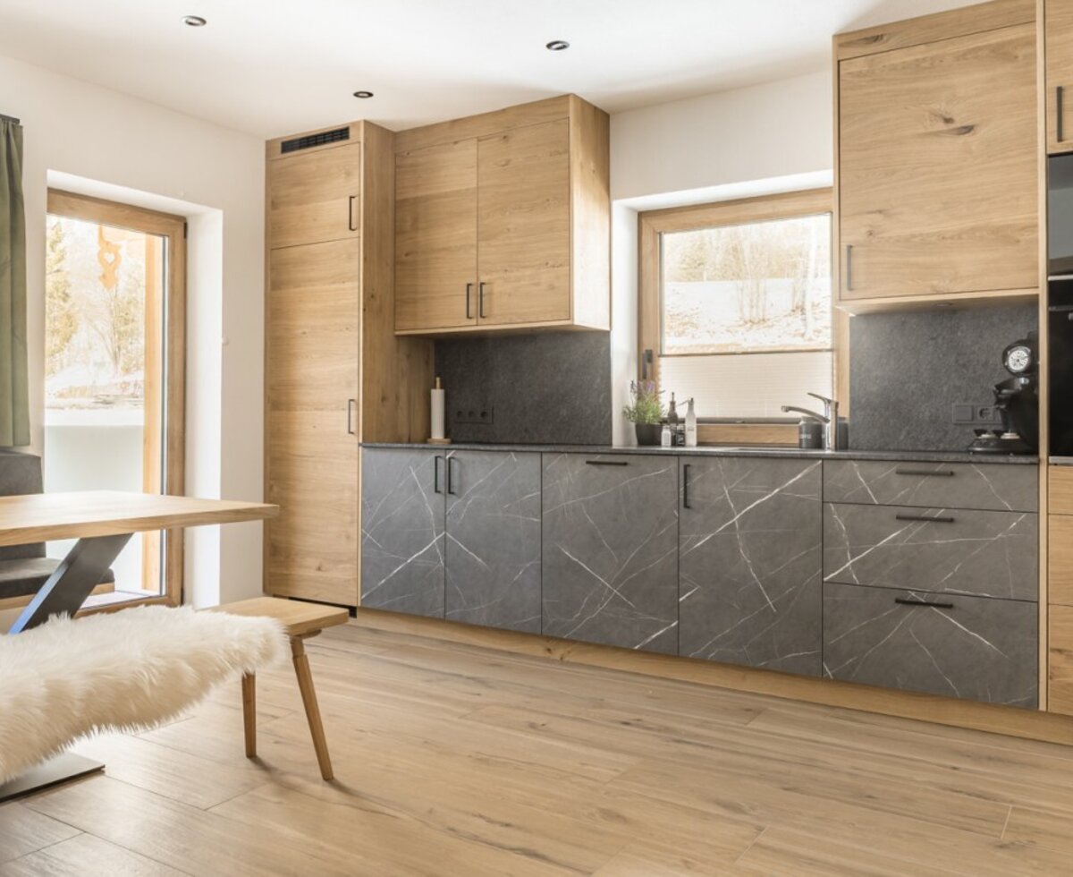 Modern kitchen with wooden elements, dark countertops, integrated appliances, and a dining table with benches.