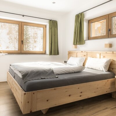 Double bedroom with a wooden bed, wooden floor, and two windows.