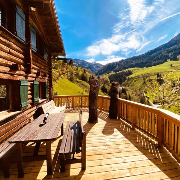 Sunny wooden terrace of the Alm with a cozy seating area and scenic views of the surrounding mountains.