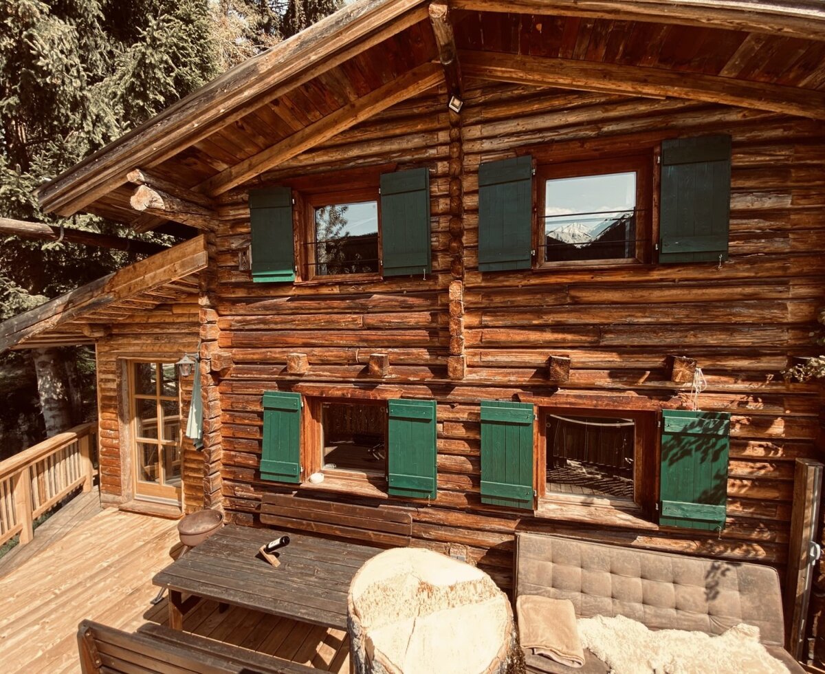 The rustic Alm made of natural wood with an inviting wooden terrace and green shutters.