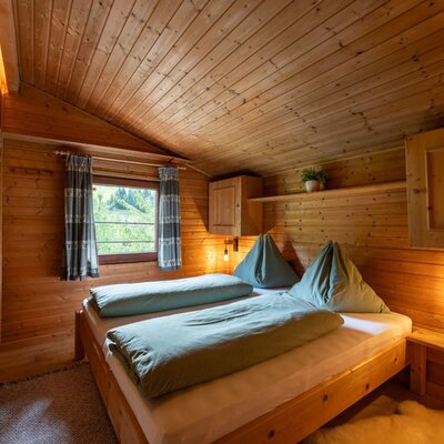 A cozy bedroom in the Alm featuring rustic wood paneling, inviting beds, and warm lighting.