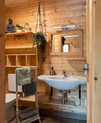 A cozy bathroom of the Alm featuring light wooden walls, a washbasin, and a practical towel rack.
