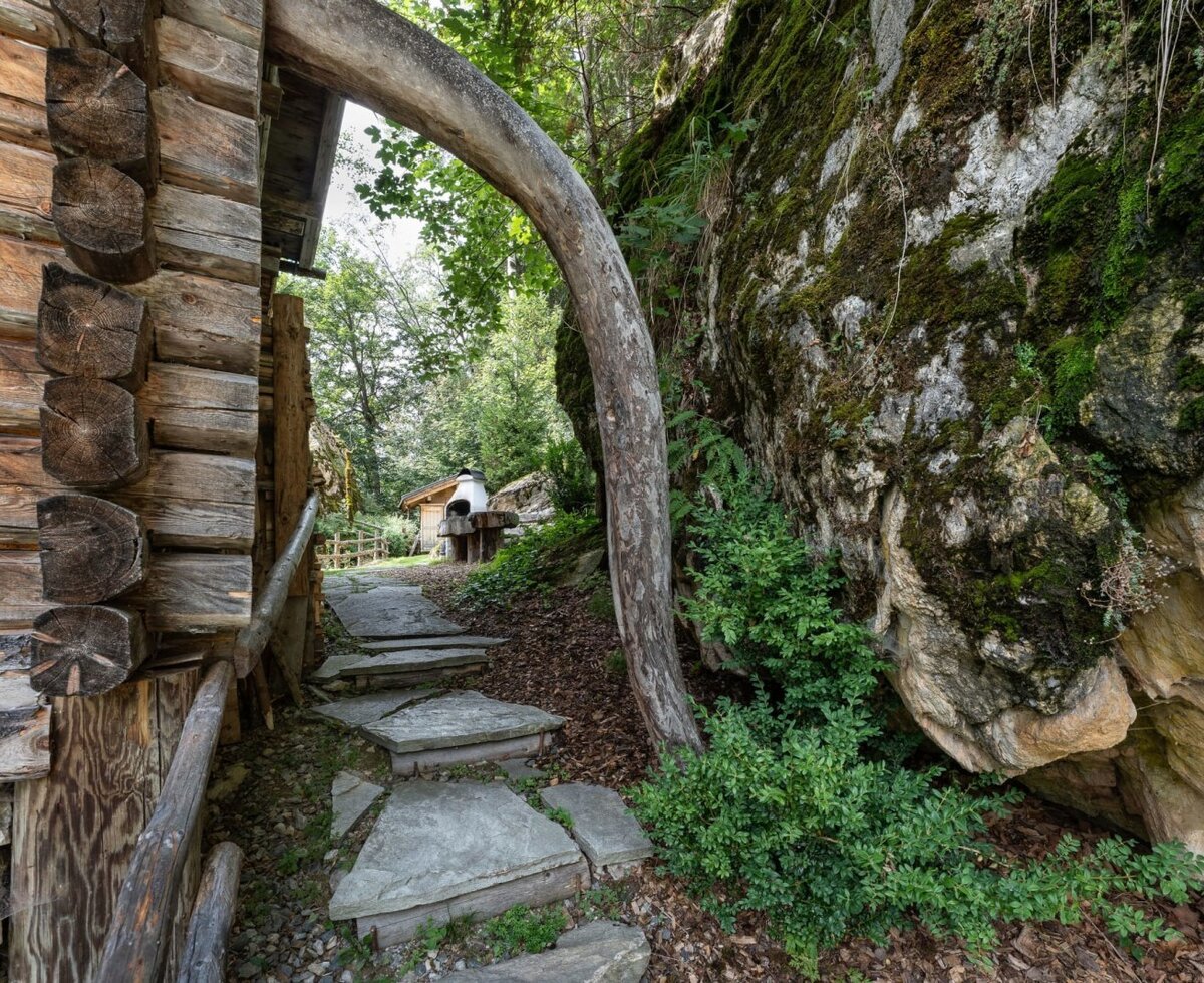 A rustic stone path along the side of the alm, surrounded by natural rock faces and lush greenery.