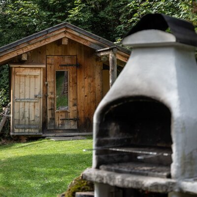 The Alm's inviting outdoor area featuring a stone barbecue and a rustic wooden cabin in the background.