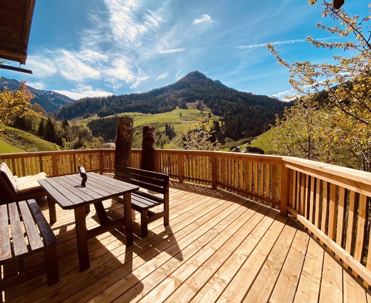 The Alm's spacious sun terrace with comfortable wooden seating and panoramic views of the surrounding mountains.