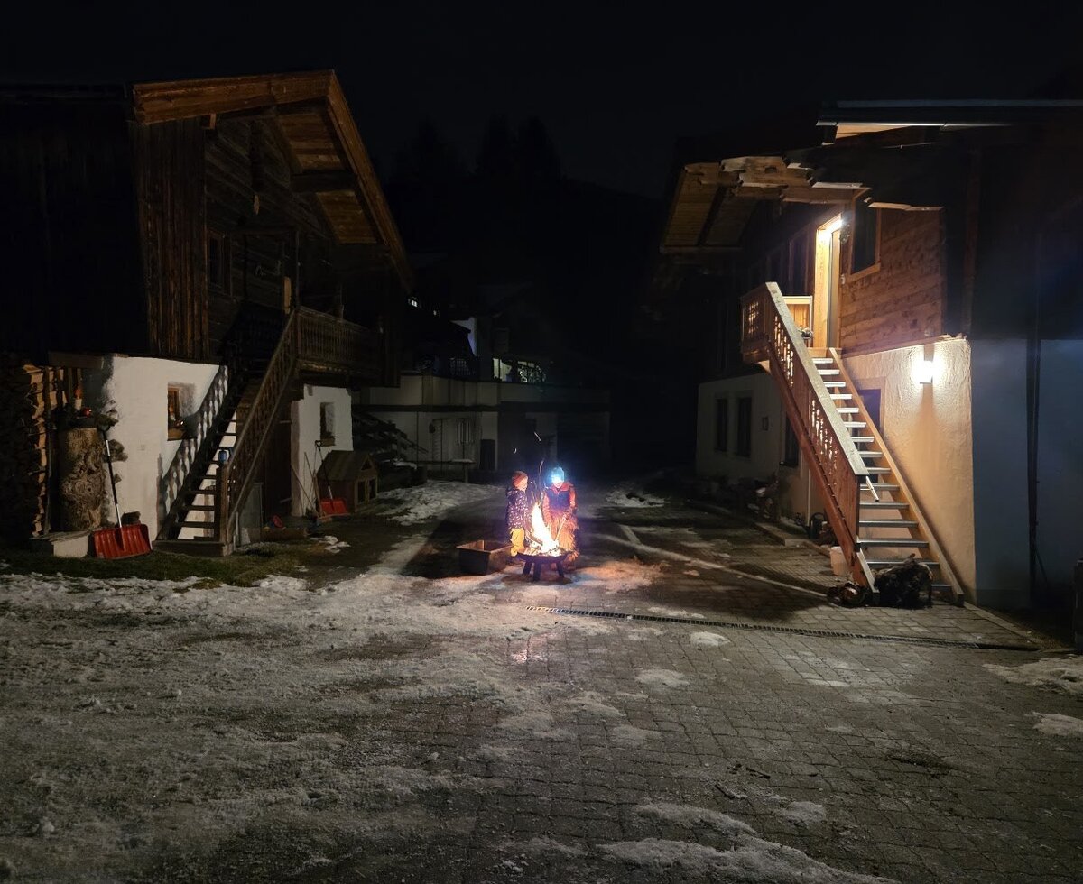 A cozy campfire in the snow-covered courtyard of the farmhouse at night.