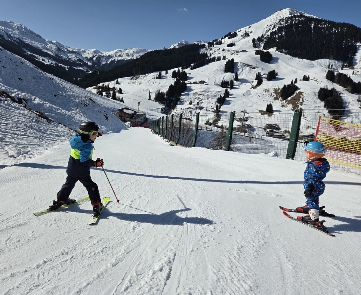 The sunny ski slope near the farmhouse offers children fun on the snow against a scenic mountain backdrop.