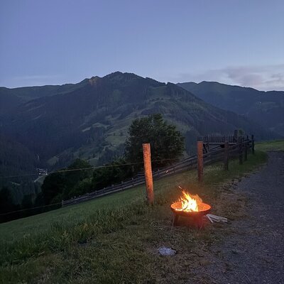 A cozy fire pit on the farmhouse grounds with scenic views of the surrounding mountains at dusk.