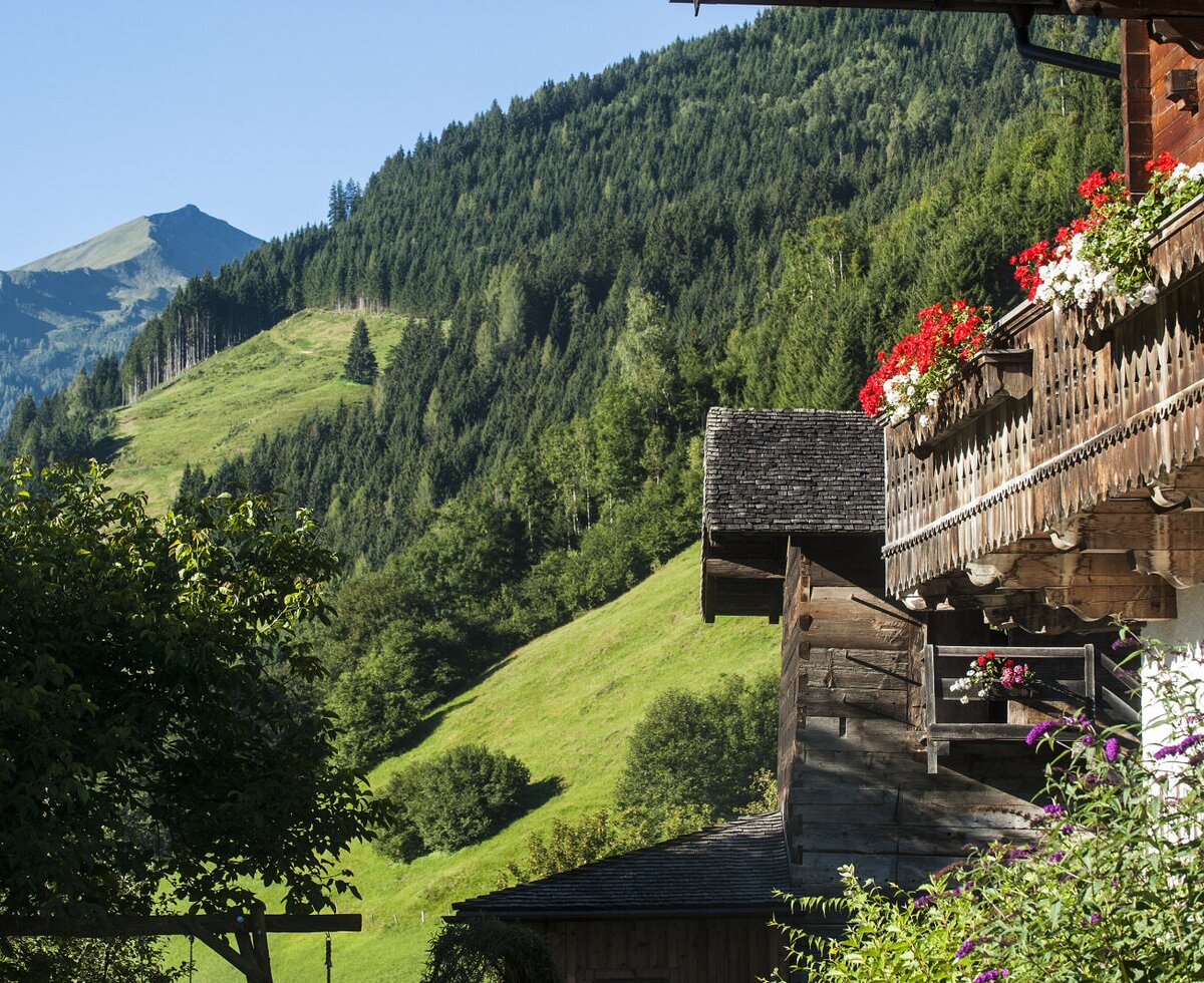 The Farm House exterior shows traditional wooden balconies decorated with red and white flowers, overlooking green mountains.