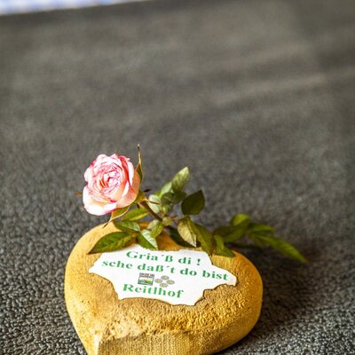 A heart-shaped wooden decoration featuring a pink rose and a welcome note for guests at the Reitlhof farm house.