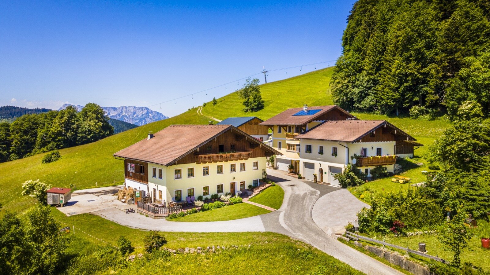 The Reitlhof Farm House, featuring several buildings, is located on a green hillside with distant mountain views.