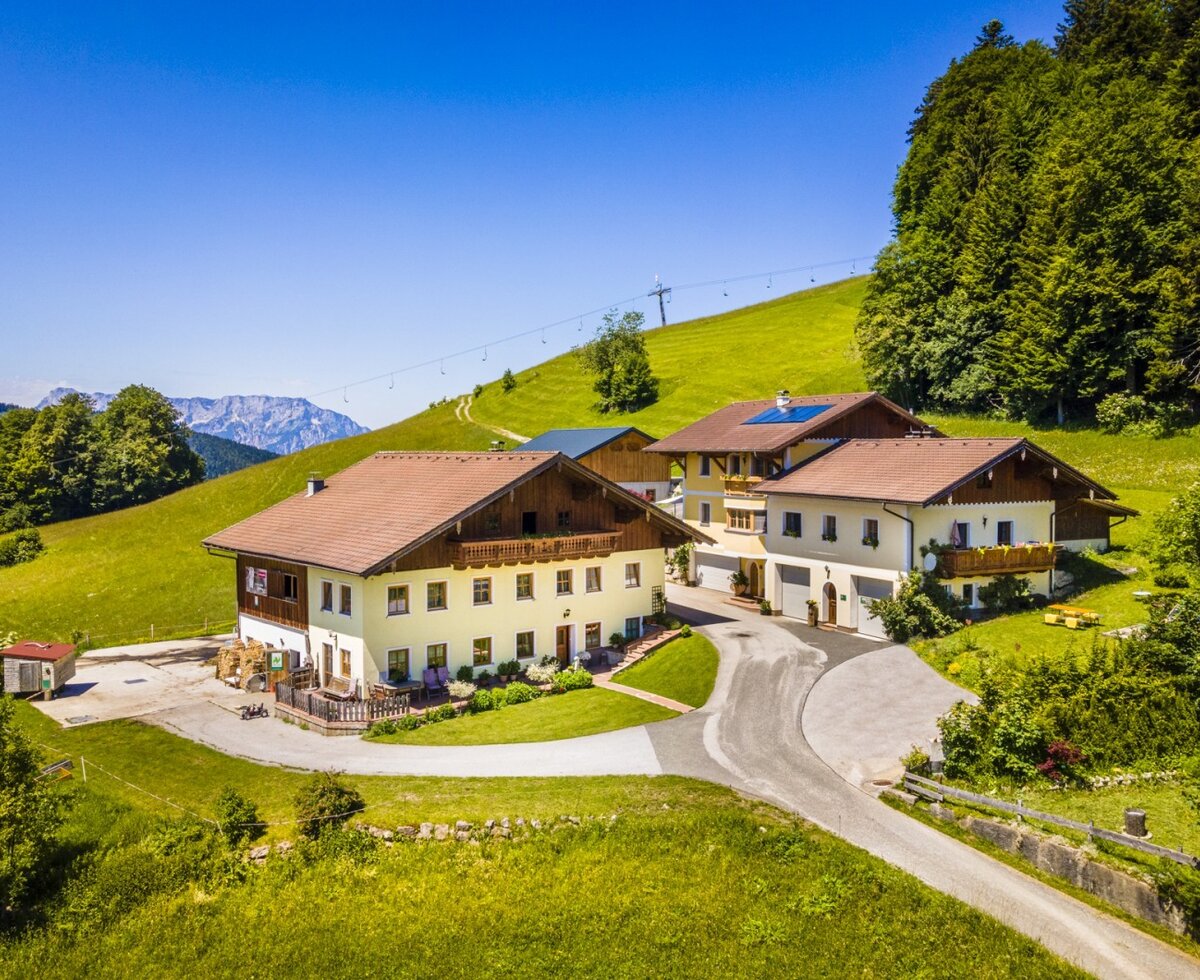 The Reitlhof farmhouse with its traditional buildings, surrounded by green meadows and mountains.