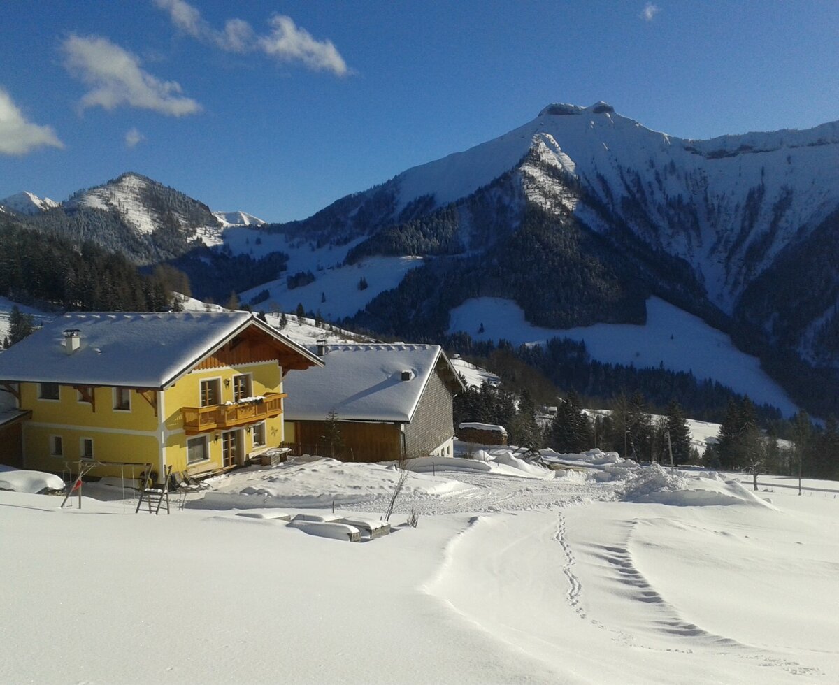 The Reitlhof farmhouse, a yellow building with balconies, set in a snow-covered landscape with the Salzburg Alps in the background.