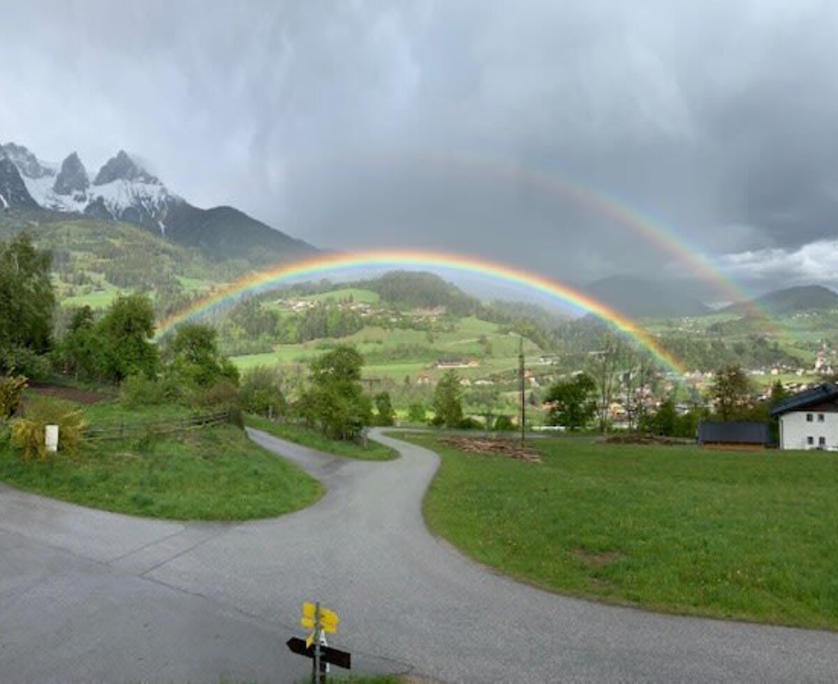 The rural view from the Farm House, featuring snow-capped mountains, green valleys, a village, and a full rainbow.