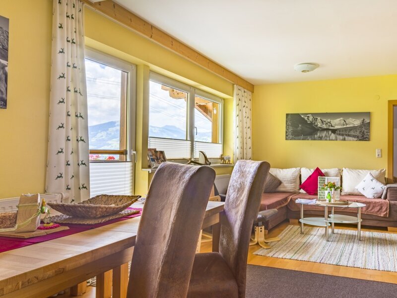 Open-plan living and dining area in the Farm House, featuring a wooden table, sofa, TV, and mountain views from the windows.