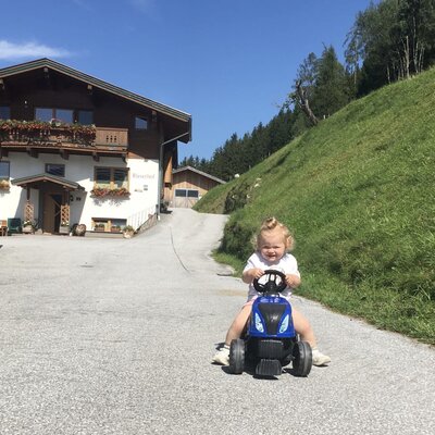 A child rides a toy tractor in front of the farmhouse, which offers child-friendly facilities.