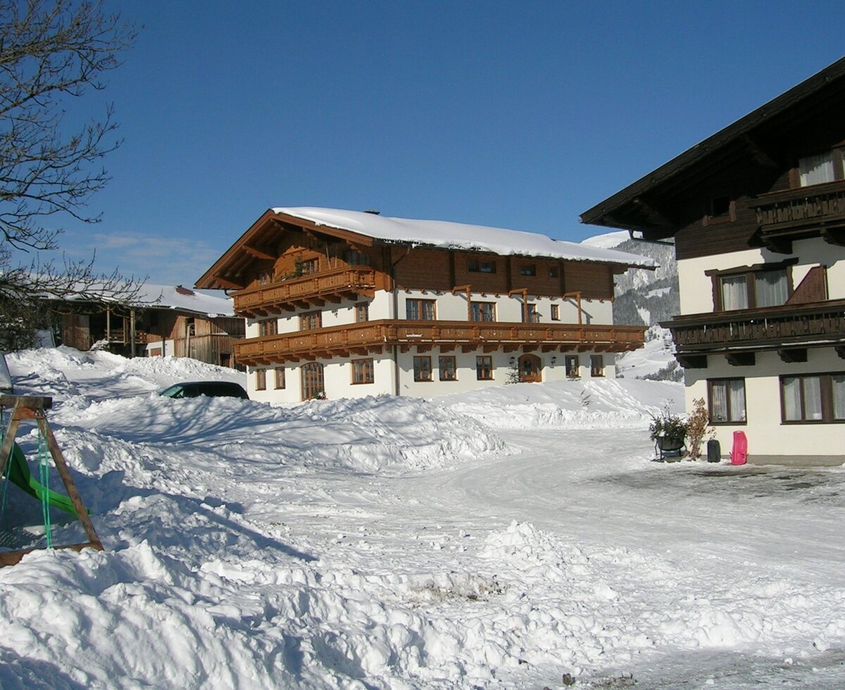 The farm house exterior in winter, with snow covering the roofs and surrounding grounds.