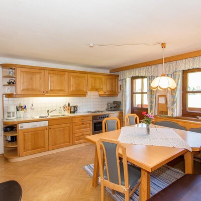 The kitchen and dining area of the farm house features wooden cabinets, a stovetop, oven, dishwasher, a dining table with a corner bench, and a wood-burning stove.
