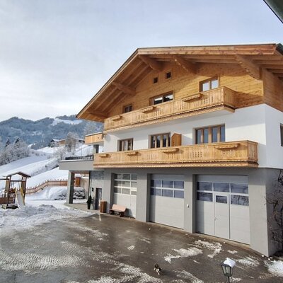 The Farm House with wooden balconies, a children's playground, and a snow-covered mountain backdrop.
