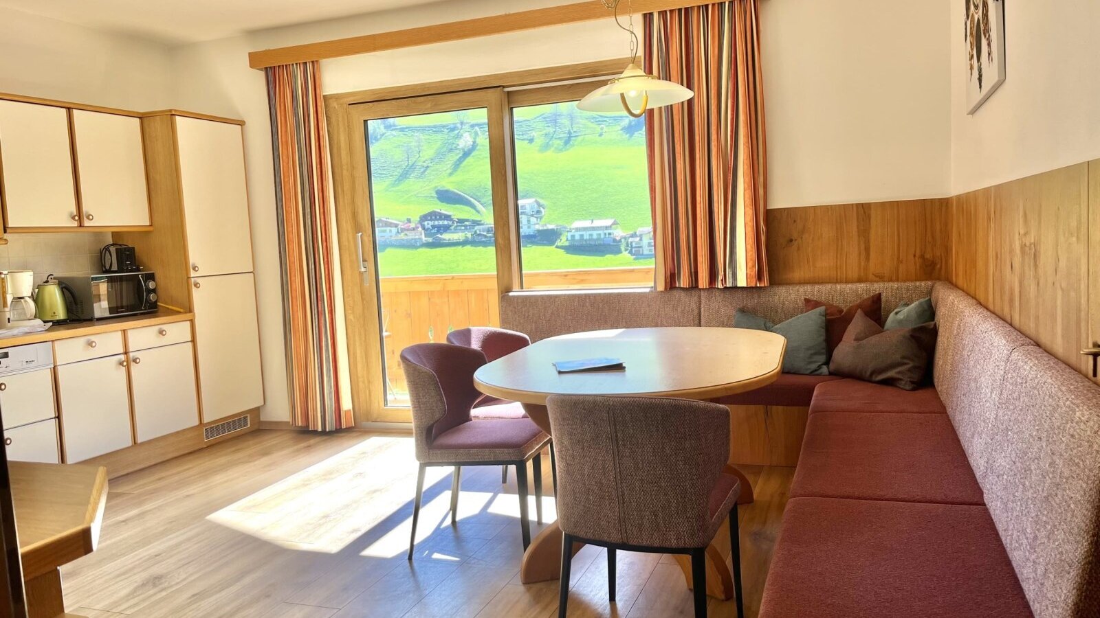 Open-plan living area in the Bauernhof with a fully equipped kitchen, dining area with a corner bench, and access to the balcony with mountain views.