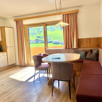 Open-plan living area in the Bauernhof with a fully equipped kitchen, dining area with a corner bench, and access to the balcony with mountain views.
