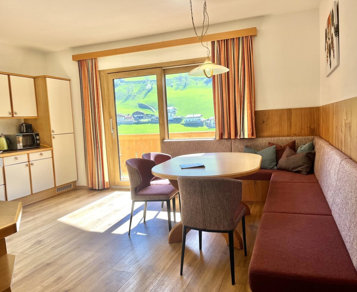Open-plan living area in the Bauernhof with a fully equipped kitchen, dining area with a corner bench, and access to the balcony with mountain views.