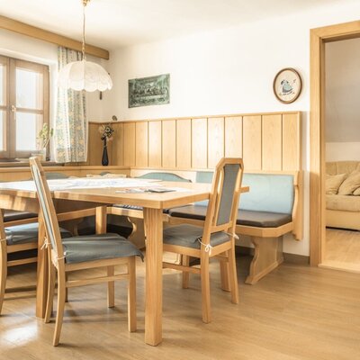 Dining area in the farmhouse with a wooden table, chairs, a corner bench, and access to another room.
