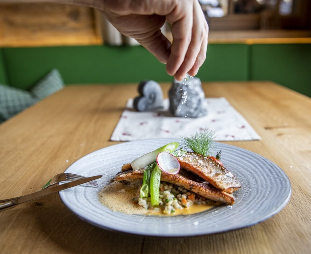 A plate of fish and vegetables being seasoned with salt on a wooden table at the farm house.