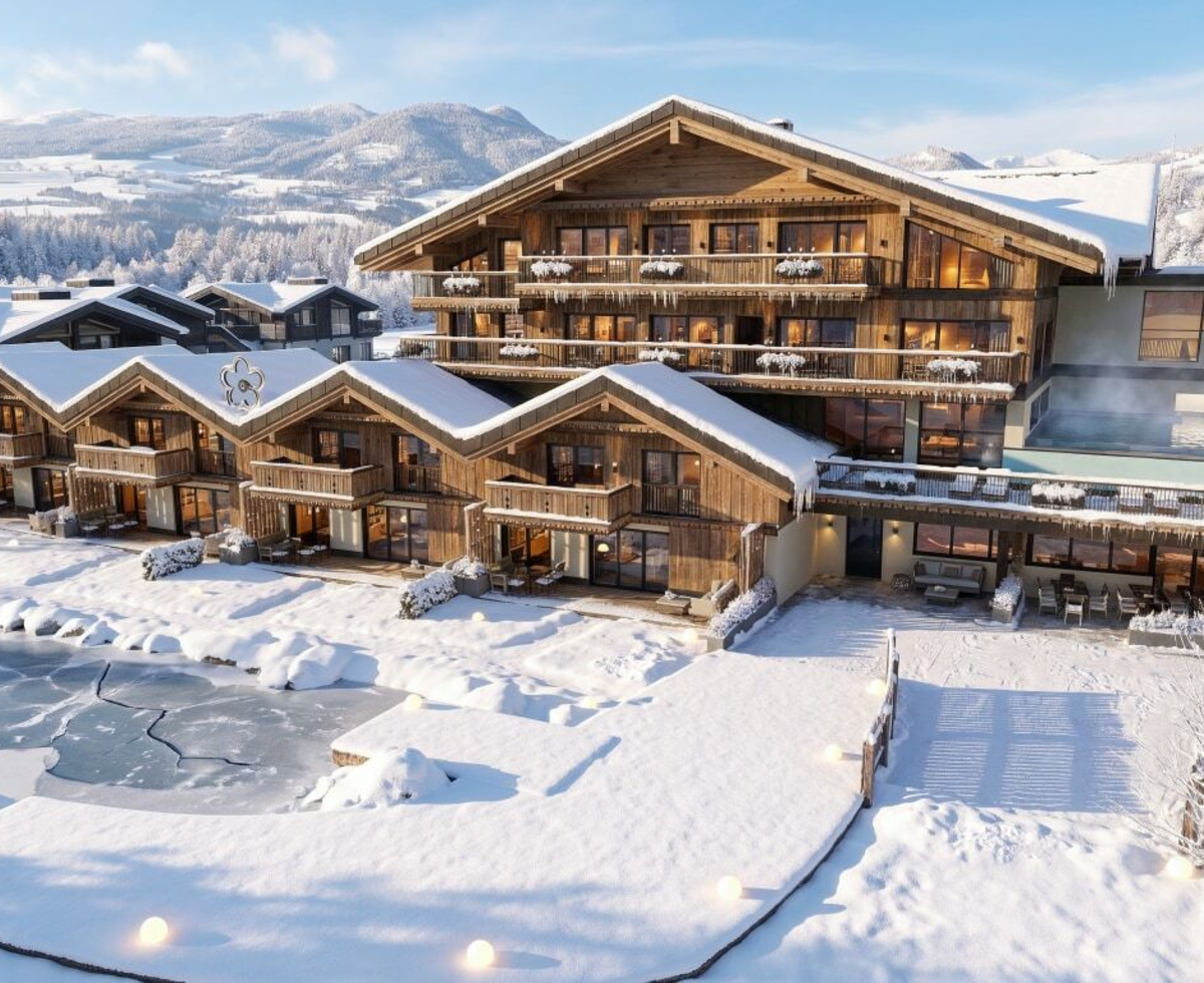Exterior view of the Bauernhof in winter, featuring multiple buildings, a heated outdoor pool, a water slide, and a frozen pond.