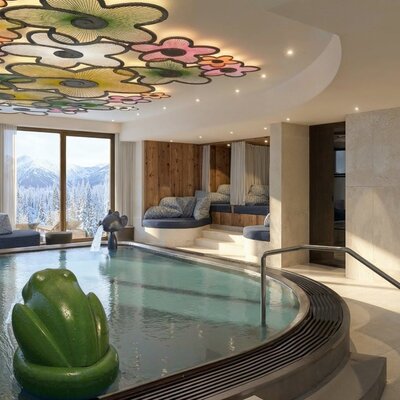 The indoor pool area of the farmhouse features a slide, a frog toy, lounging areas, a decorative ceiling, and panoramic views of the snowy mountains.