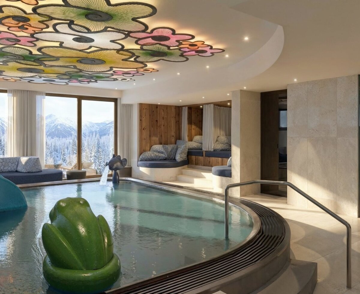 The indoor pool area of the farmhouse features a slide, a frog toy, lounging areas, a decorative ceiling, and panoramic views of the snowy mountains.