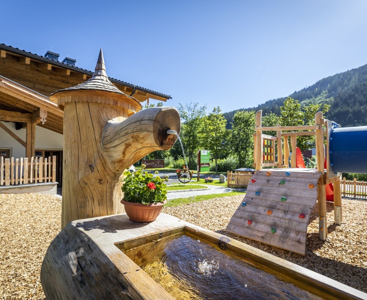 The children's playground at the Farm House includes a climbing wall, slide, and a wooden water feature.