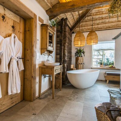 The Farm House bathroom offers a freestanding bathtub, wooden vanity, exposed ceiling beams, and bathrobes for guest use.