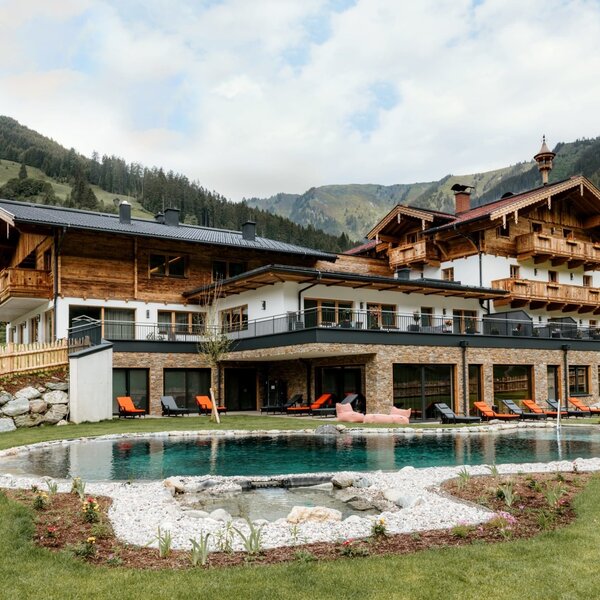 The farm house features an outdoor swimming pool surrounded by a green lawn and sun loungers, with mountain views.