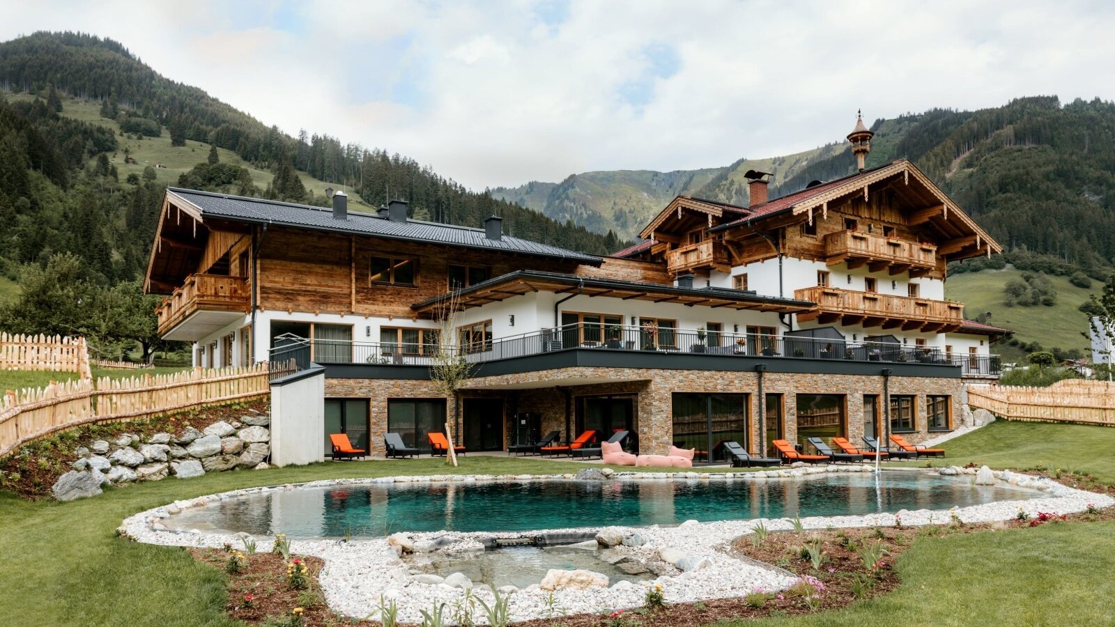 The farm house features an outdoor swimming pool surrounded by a green lawn and sun loungers, with mountain views.