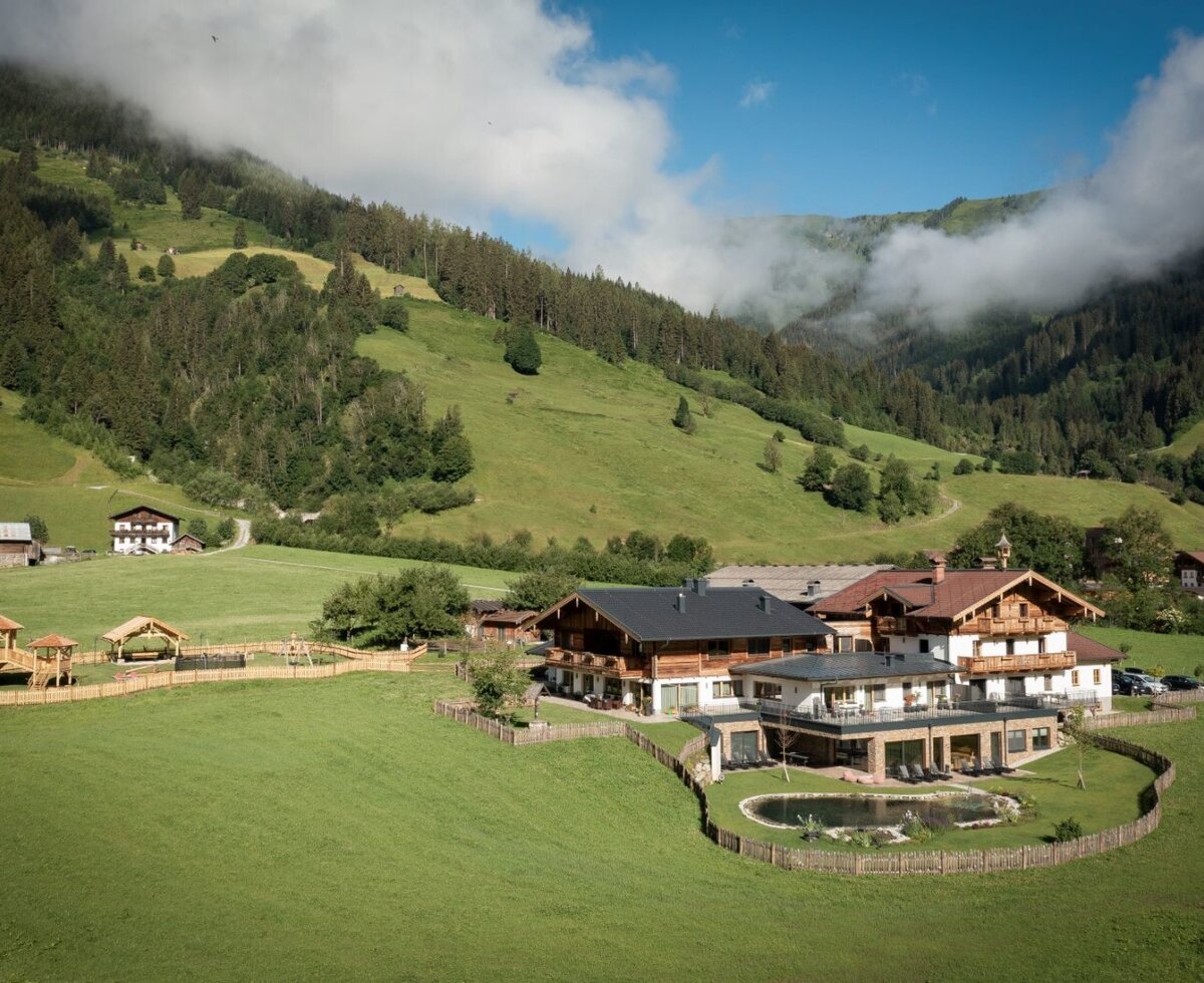 The Farm House property features a natural swimming pond and a children's playground, set within a green mountain valley.