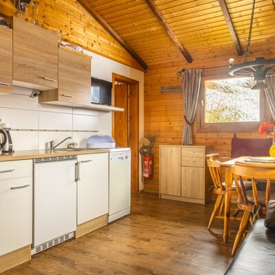 Farmhouse kitchen area with a stovetop, sink, and dishwasher, alongside a dining area featuring a wooden table and bench seating.