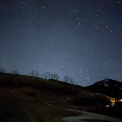 The clear starry sky above the almhut, surrounded by dark mountains and hills at night.