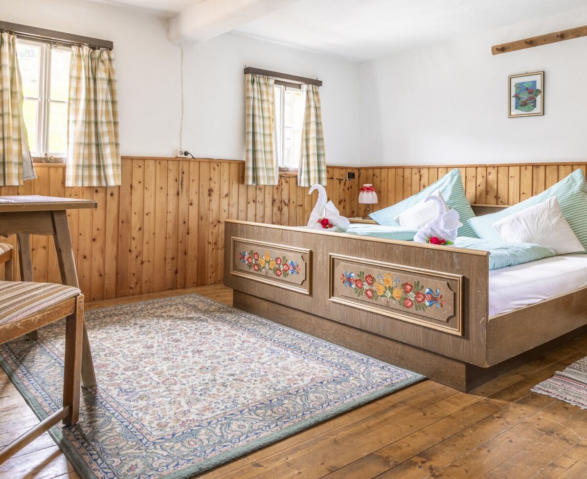 Bedroom in the farmhouse featuring a bed with a decorative painted frame, wood paneling, and a desk with a chair.