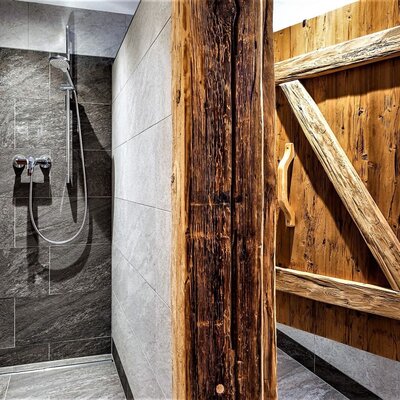 Shower in the farmhouse bathroom featuring dark grey stone-effect tiles, a rain shower head, and rustic wooden privacy screens.
