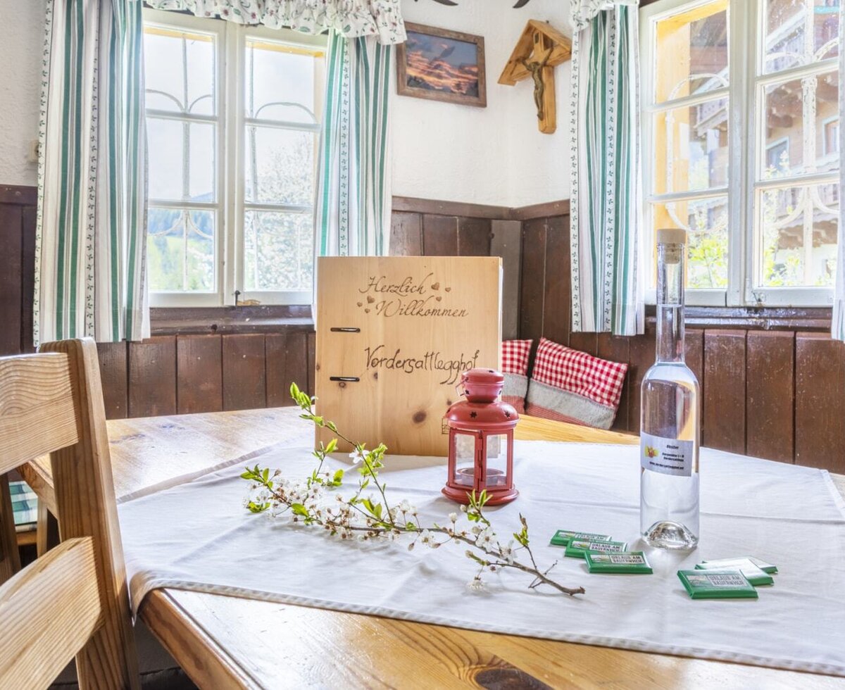 The farmhouse dining table is set with a welcome sign, a decorative branch, and a bottle, positioned by windows with striped curtains.