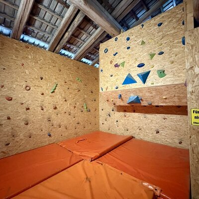 An indoor bouldering wall with safety mats, available as a recreational facility for guests at the farmhouse.