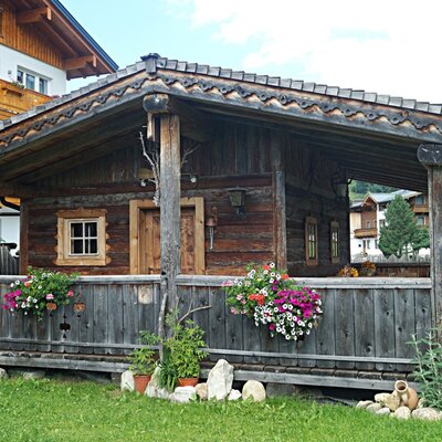 A rustic wooden building on the Farm House grounds, featuring a covered porch with decorative flower boxes.