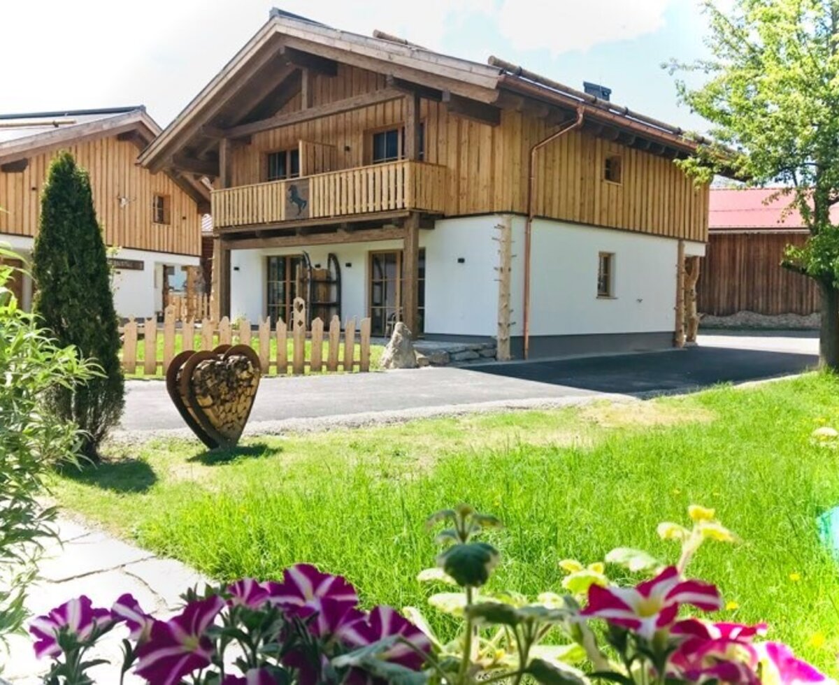 The Farm House exterior with its wooden upper level, white lower level, a balcony, and a front lawn with flowers.