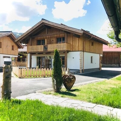 The main farm house features traditional wooden and white-painted exterior walls, a balcony, and a small fenced garden area.