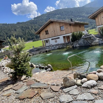 The natural swimming pond at the Farm House features water jets, a handrail for entry, and stone landscaping with mountain views.