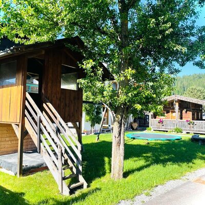 The outdoor play area at the Farm House includes a wooden playhouse with stairs and a trampoline on a grassy lawn.