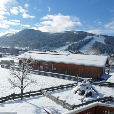 View from the farmhouse of the snowy winter landscape with a ski slope and surrounding buildings.